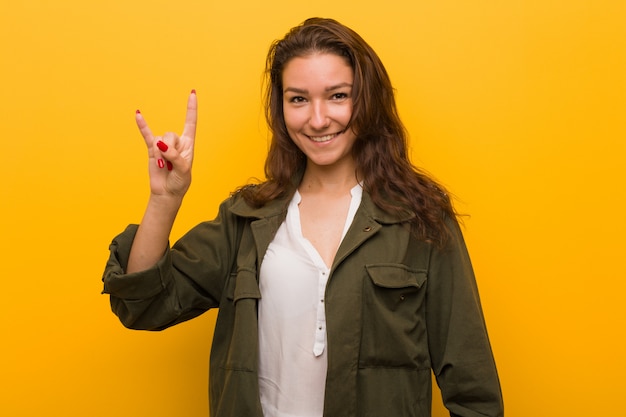 Mujer europea joven aislada sobre el amarillo que muestra un gesto de los cuernos como concepto de la revolución.