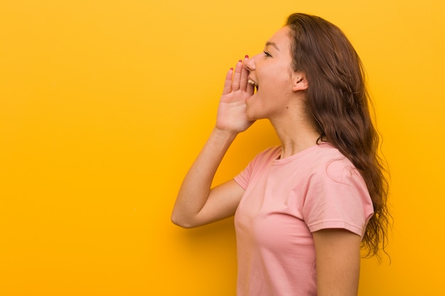 Mujer europea joven aislada sobre fondo amarillo que grita y que sostiene la palma cerca de boca abierta.