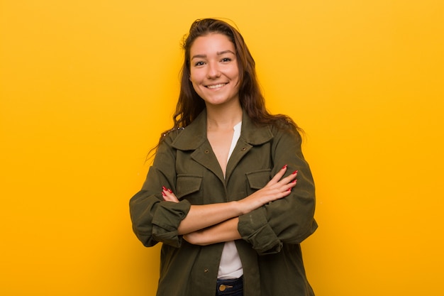 Foto mujer europea joven aislada sobre el fondo amarillo que sonríe confiado con los brazos cruzados.