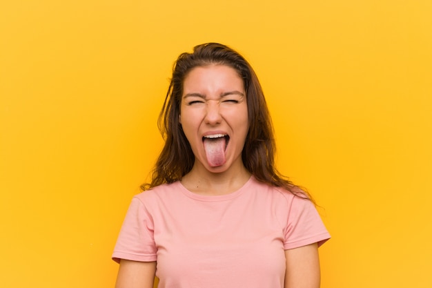 Mujer europea joven aislada sobre la pared amarilla divertida y amistosa sacando la lengua.