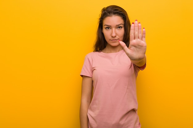 Mujer europea joven aislada sobre la situación amarilla con la mano extendida que muestra la muestra de la parada, previniéndole.