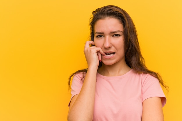 Mujer europea joven aislada sobre las uñas amarillas que muerden, nerviosas y muy ansiosas.