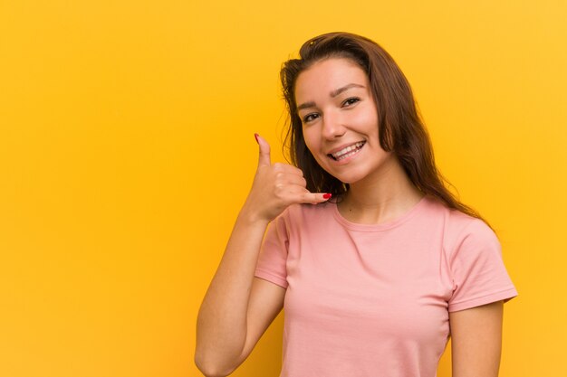 Mujer europea joven sobre la pared amarilla que muestra un gesto de llamada de teléfono móvil con los dedos.