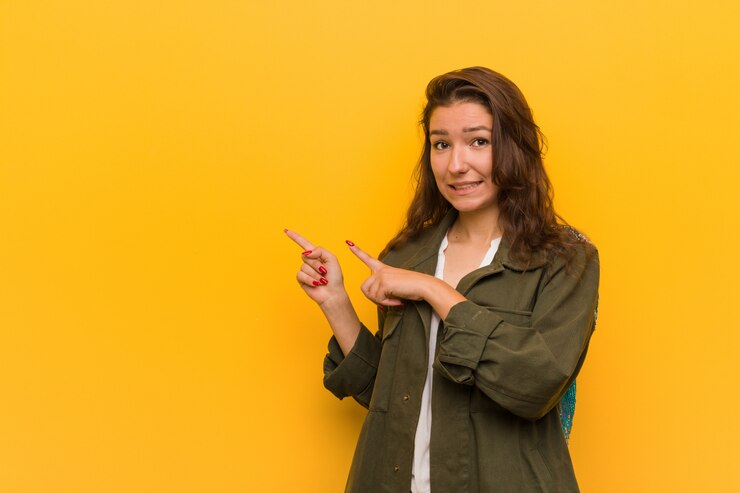 Foto la mujer europea joven sobre la pared amarilla sorprendió señalar con los dedos índices a un espacio en blanco.