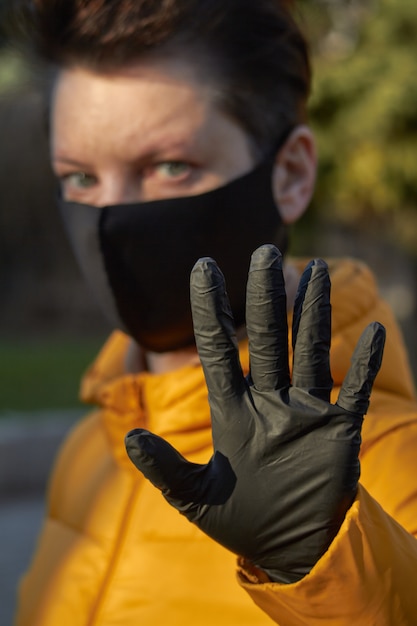 Mujer europea de mediana edad con máscara negra protectora hace un gesto de advertencia durante la epidemia de coronavirus COVID-19. Mujer enferma con protección durante la pandemia.
