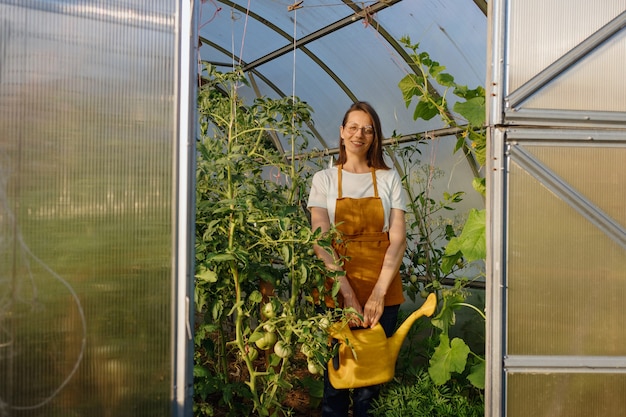 Una mujer europea con una regadera amarilla está regando frutas y verduras en su jardín un