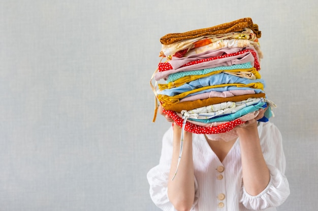 Una mujer europea tiene una gran cantidad de ropa de colores en sus manos para lavar en la lavandería o reciclar