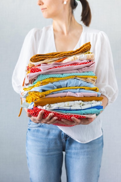 Una mujer europea tiene una gran cantidad de ropa de colores en sus manos para lavar en la lavandería o reciclar