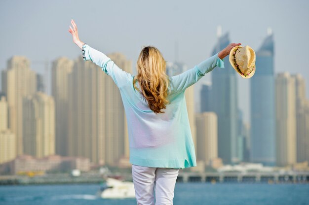 La mujer europea Yang posa en una valla de piedra frente a la ciudad moderna junto al mar