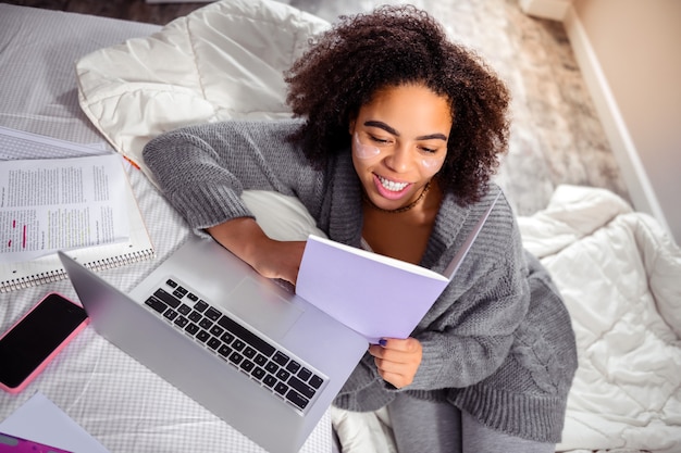 Mujer examinando papeles. Sonriente dama alegre leyendo conspectus mientras tiene tiempo de trabajo en su cama