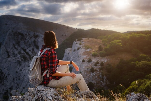 Mujer excursionista disfruta de la vista en el acantilado del pico de la montaña al atardecer