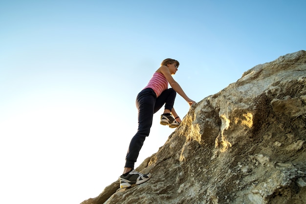 Mujer excursionista escalada empinada gran roca en un día soleado