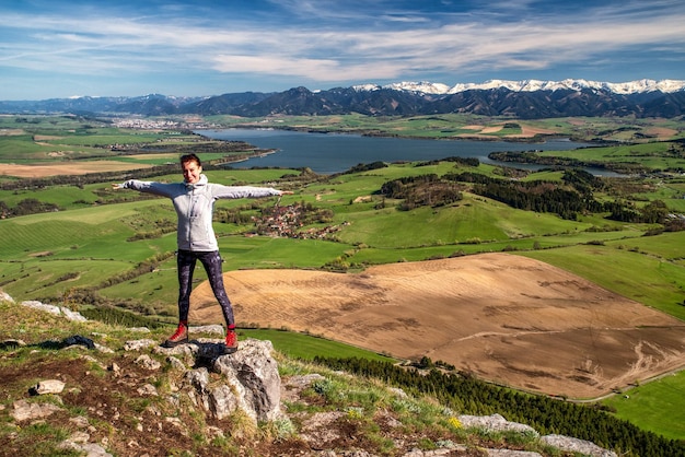 Mujer excursionista feliz en la cima de la colina con un hermoso paisaje primaveral en el fondo