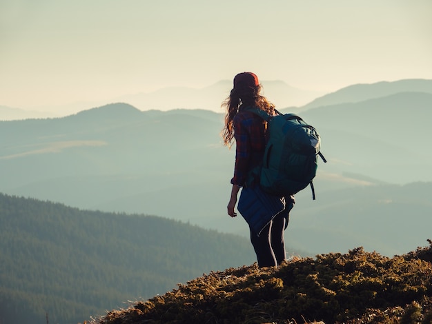 Mujer excursionista con mochila en la cima de una montaña con fondo de montañas