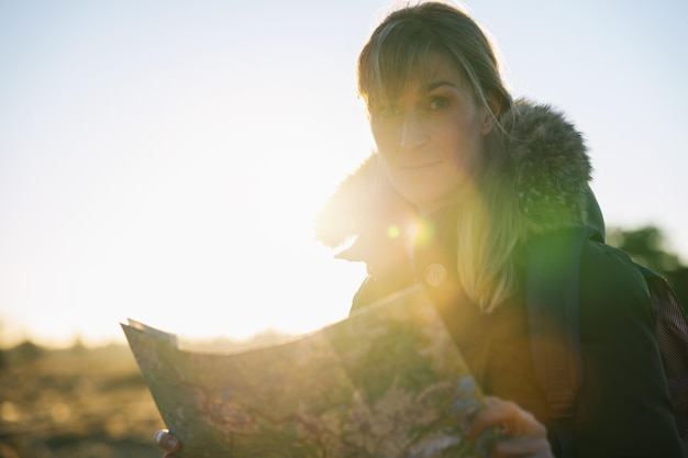 Foto mujer excursionista con una mochila y un mapa buscando la dirección correcta en el desierto al atardecer