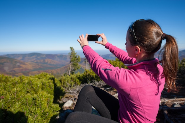 Mujer excursionista tomando foto en la cima de la montaña