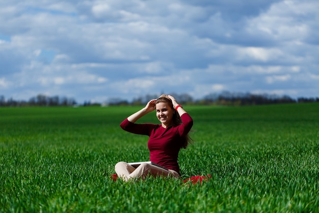 Mujer de éxito joven está sentada sobre la hierba verde con una computadora portátil en sus manos. Descanse después de una buena jornada laboral. Trabaja en la naturaleza. Chica estudiante trabajando en un lugar apartado. Lugar de trabajo en la naturaleza