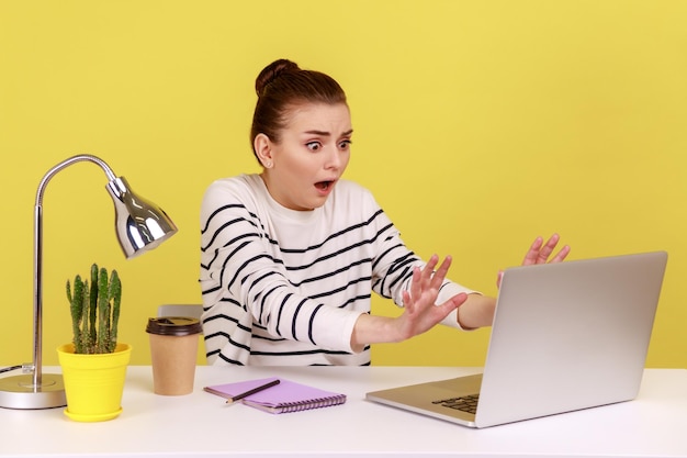 Mujer con expresión conmocionada levantando las manos en gesto de parada trabajando en contenido prohibido en computadora portátil