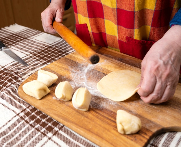 Mujer extendiendo la masa con un rodillo sobre la mesa de la cocina.