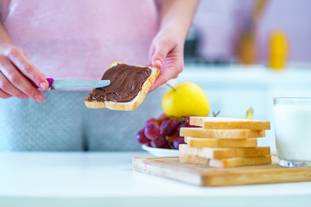 Mujer extiende mantequilla de chocolate con nueces sobre pan tostado para un postre