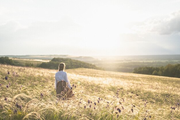 Foto mujer con falda larga se para en un campo dorado y mira la puesta de sol