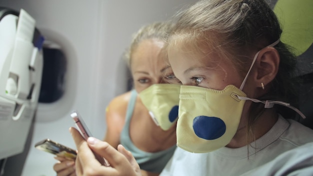 Mujer de familia y niño bebé viajan turista caucásico en avión con máscara médica protectora Leer noticias impactantes sobre el coronovirus en el teléfono inteligente Epidemia de virus sarscov2 covid19