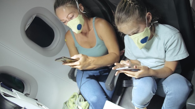 Mujer de familia y niño bebé viajan turista caucásico en avión con máscara médica protectora Leer noticias impactantes sobre el coronovirus en el teléfono inteligente Epidemia de virus sarscov2 covid19