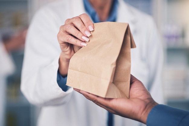 Mujer farmacéutica y manos con bolsa de papel para la atención médica del paciente o medicamentos en la farmacia Primer plano de una mujer o profesional médico que da pastillas, medicamentos o productos farmacéuticos al cliente