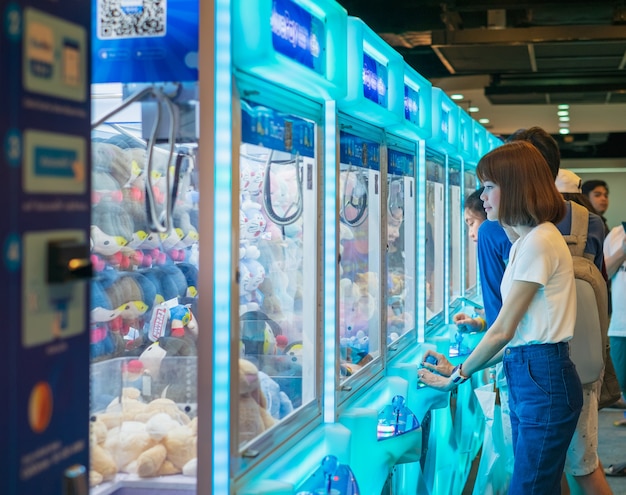 Mujer de felicidad jugando juego de garra o gabinete para atrapar a las muñecas