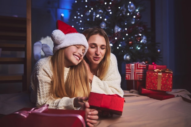 Mujer feliz abrazando a su amada hija bajo el árbol de Navidad