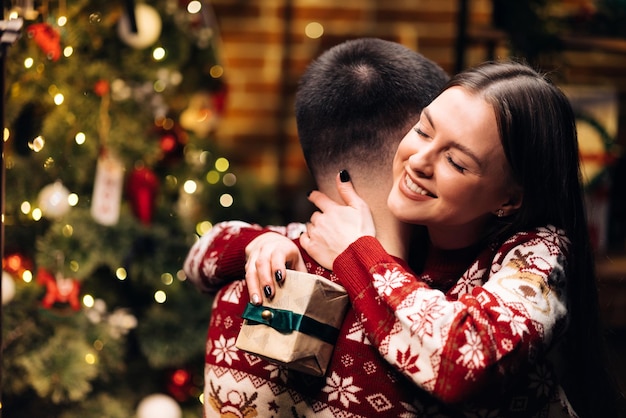 Mujer feliz abrazando a su novio y abrazándolo cerca de invierno romántico abeto decorado brillante