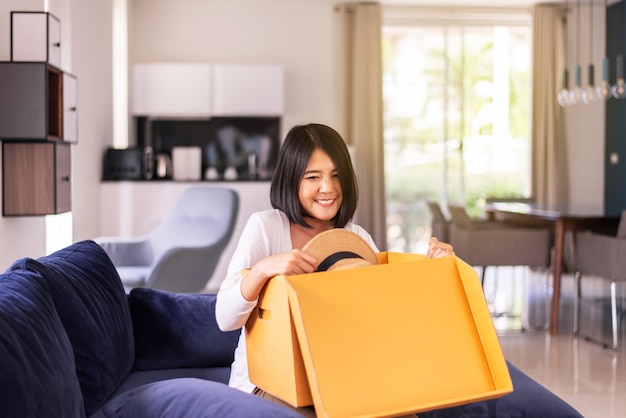 Mujer feliz abriendo una caja de regalo mientras está sentado en el sofá en casa, día sorpresa