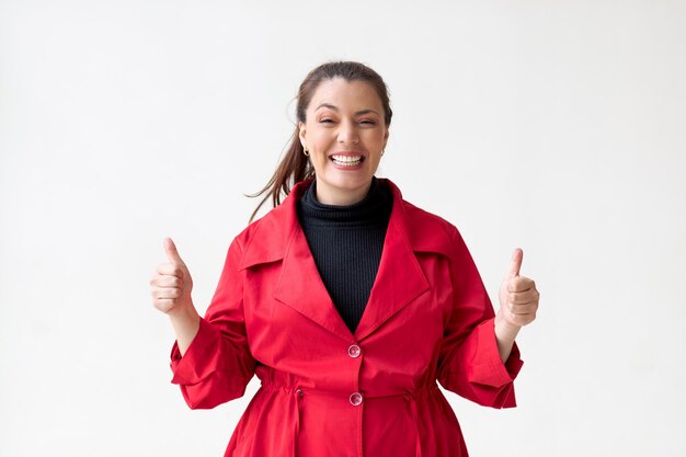 Foto mujer feliz con abrigo rojo sobre fondo blanco con los pulgares levantados