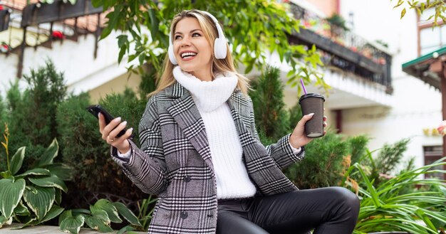 Mujer feliz adulta durante el almuerzo en auriculares escuchando música y bebiendo café en el