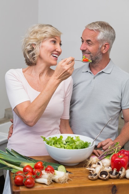 Mujer feliz alimentando ensalada de pareja madura en la cocina