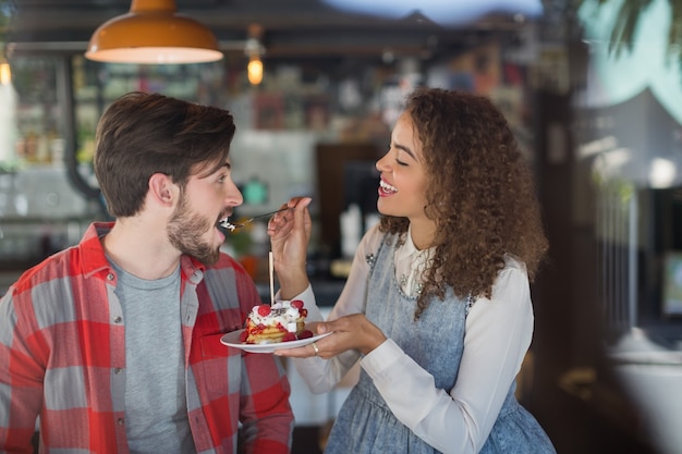 Mujer feliz alimentando pastel a amigo masculino