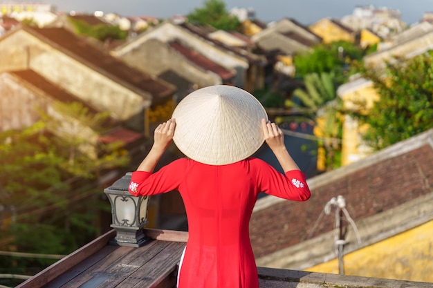 Foto mujer feliz con ao dai vestido vietnamita viajero vista turística en la azotea en hoi an, un antiguo punto de referencia de la ciudad y popular para las atracciones turísticas vietnam y el concepto de viaje del sudeste