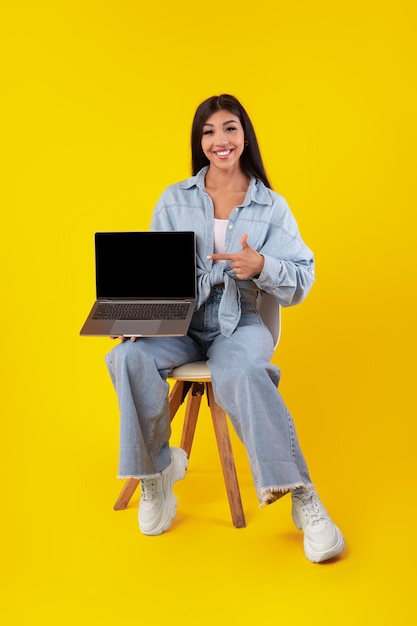 Mujer feliz apuntando a la pantalla del portátil vacía negra