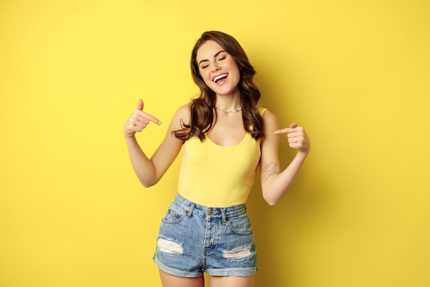 Una mujer feliz y atractiva apuntándose con el dedo a sí misma promocionando algo personal sonriendo y mirando...