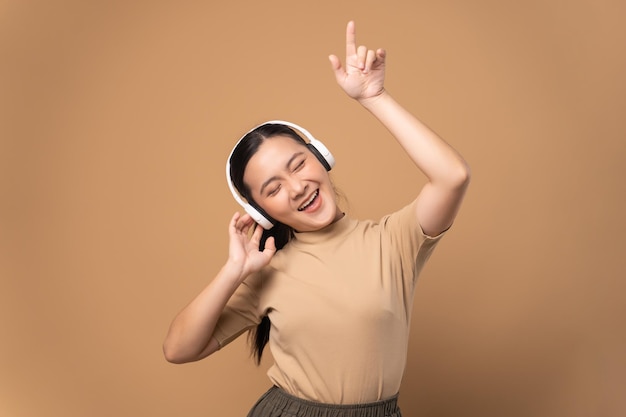 Mujer feliz con auriculares y escuchando música aislada de fondo beige