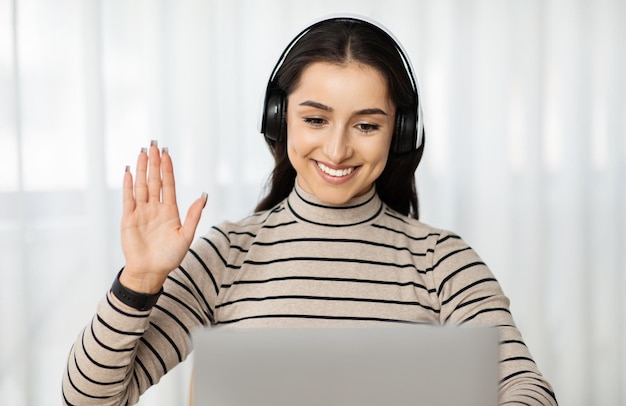 Mujer feliz con auriculares en el uso de computadora portátil para una llamada de video ondas a la pantalla