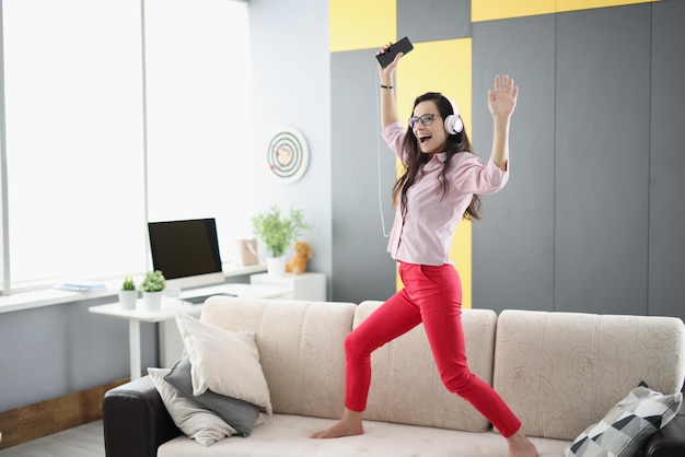 Mujer feliz bailando en el sofá escuchando música en auriculares y cantando