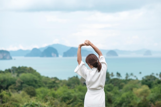 Mujer feliz en bata de baño estirándose después de despertarse y disfrutar de la vista al mar Turista relajándose en un resort tropical viajes de verano vacaciones y concepto de vacaciones