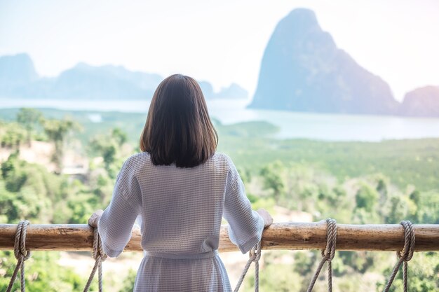 Mujer feliz en bata de baño que se extiende después de despertarse y disfrutar del punto de vista de la bahía de Phang Nga