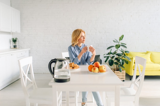 Mujer feliz bebe café con leche, desayuno en la cocina. Persona femenina en casa por la mañana, nutrición saludable y estilo de vida