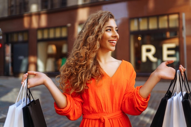 Mujer feliz con bolsas de compras caminando por la calle soleada Concepto de estilo de vida compra venta