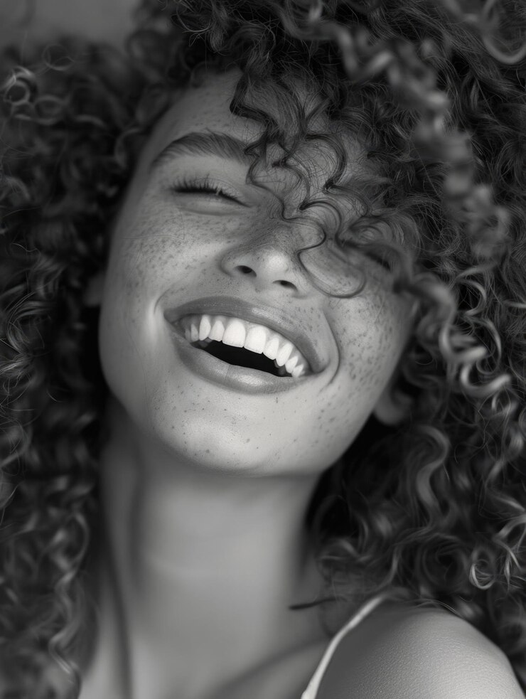 Una mujer feliz con el cabello rizado cierra los ojos y sonríe un momento de alegría capturado