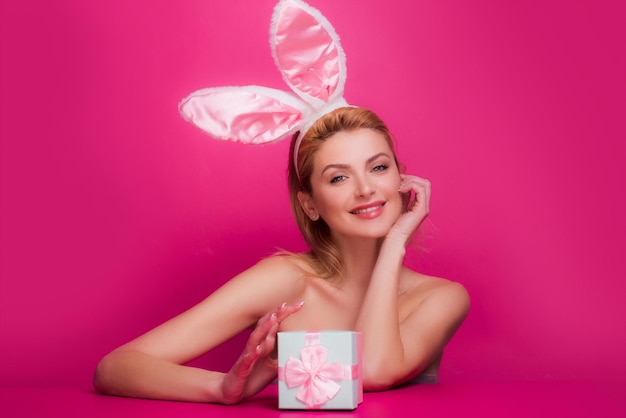 Mujer feliz con caja de regalo y orejas de conejo en celebración Pascua aislado en rosa