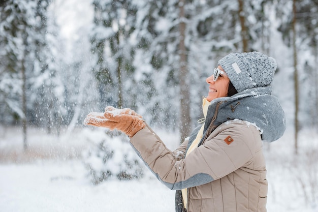 Mujer feliz caminando en el bosque de invierno durante las fuertes nevadas, viendo caer copos de nieve en el parque