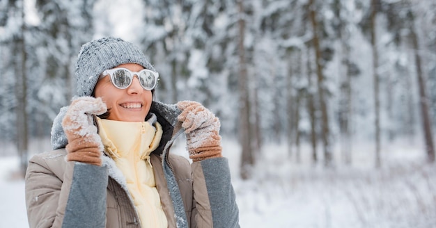 Foto mujer feliz caminando en el bosque de invierno durante las fuertes nevadas viendo caer copos de nieve en el parque